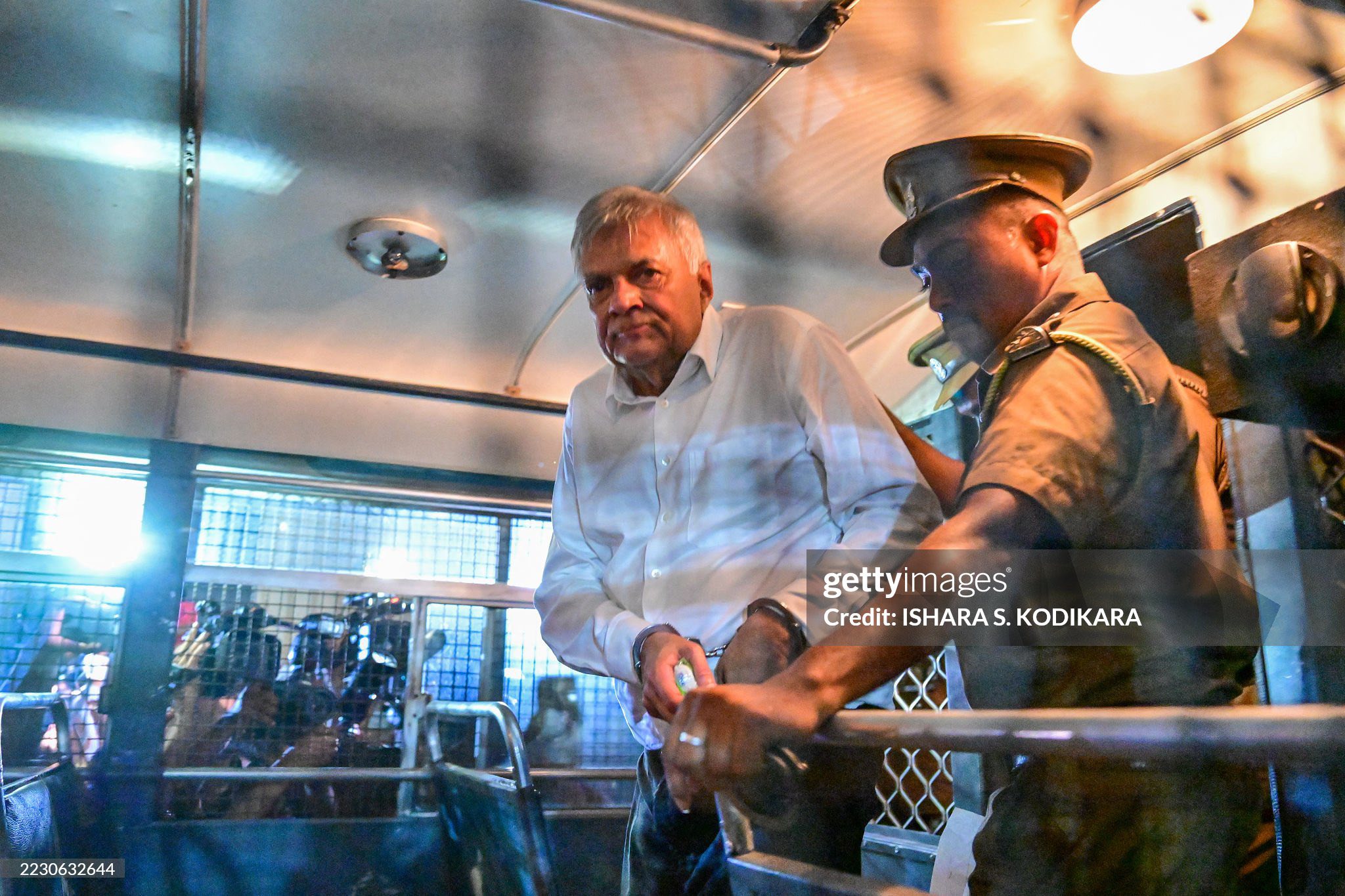 Sri Lanka's former president Ranil Wickremesinghe (L) is escorted to his seat in a prison bus in Colombo on August 22, 2025, after a magistrate ordered him to be held in remand custody till August 26, 2025, following allegations that he misused state funds to travel to Britain in 2023. (Photo by Ishara S. KODIKARA / AFP) (Photo by ISHARA S. KODIKARA/AFP via Getty Images)