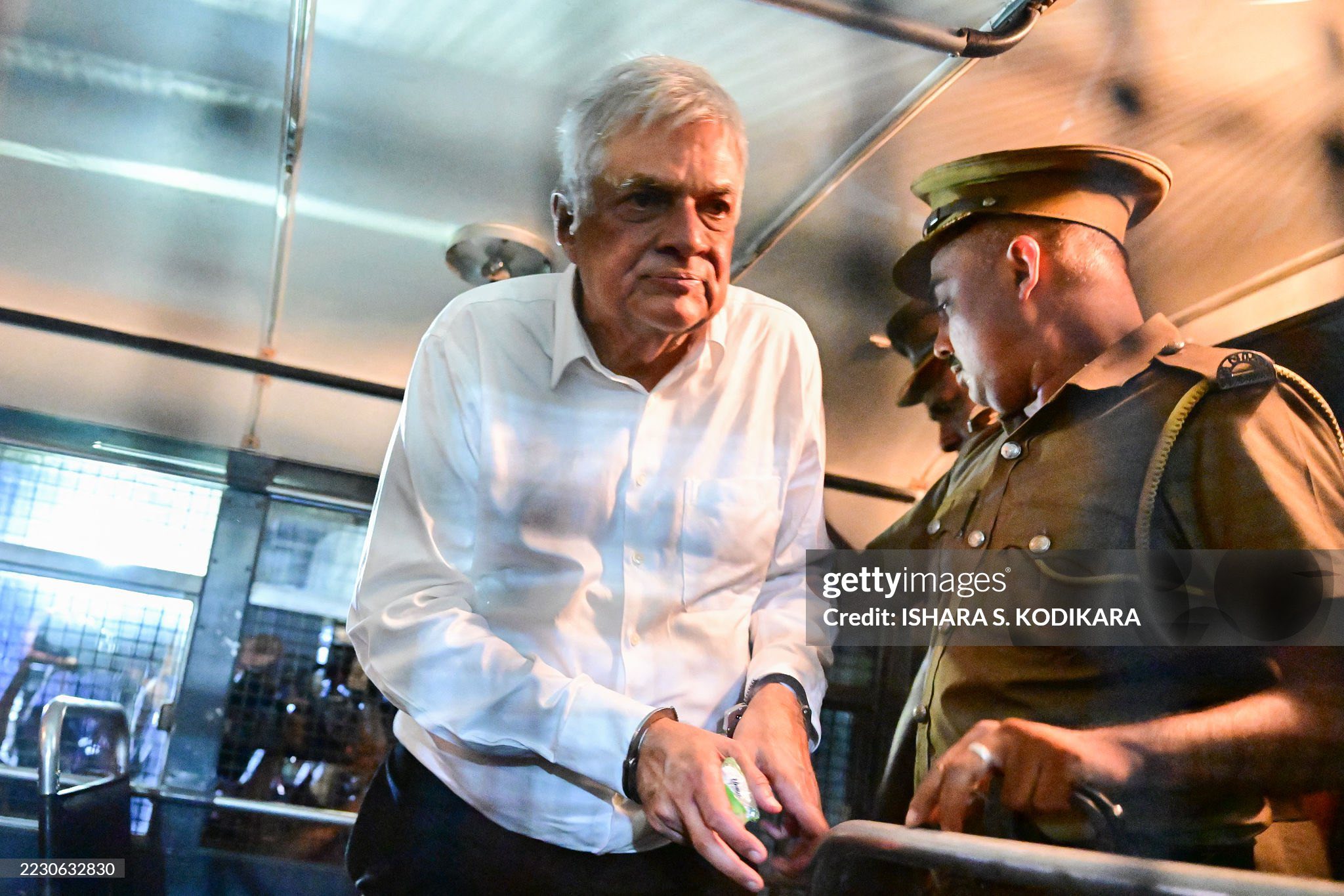 Sri Lanka's former president Ranil Wickremesinghe (L) is escorted to his seat in a prison bus in Colombo on August 22, 2025, after a magistrate ordered him to be held in remand custody till August 26, 2025, following allegations that he misused state funds to travel to Britain in 2023. (Photo by Ishara S. KODIKARA / AFP) (Photo by ISHARA S. KODIKARA/AFP via Getty Images)