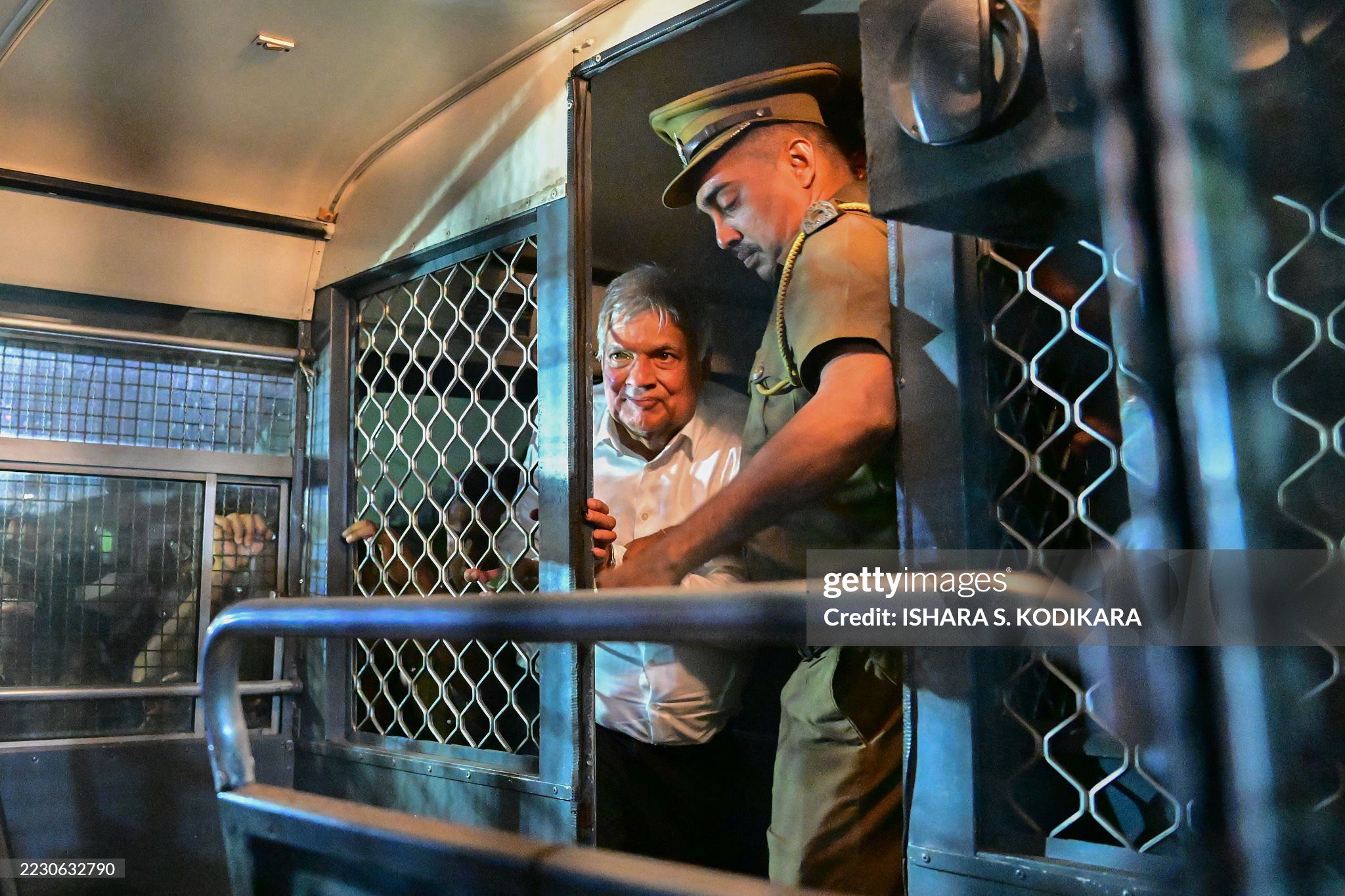 Sri Lanka's former president Ranil Wickremesinghe (L) is escorted to his seat in a prison bus in Colombo on August 22, 2025, after a magistrate ordered him to be held in remand custody till August 26, 2025, following allegations that he misused state funds to travel to Britain in 2023. (Photo by Ishara S. KODIKARA / AFP) (Photo by ISHARA S. KODIKARA/AFP via Getty Images)